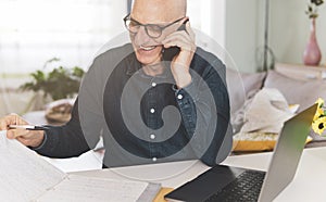 Man talking and laughing on the phone while checking work documents - Mature man working from home on the computer - Remote