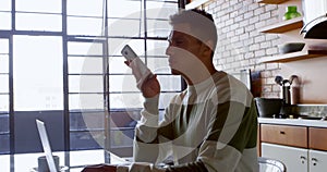 Man talking on mobile phone while using laptop in kitchen 4k