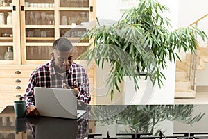 Man talking on mobile phone while using laptop on worktop in kitchen