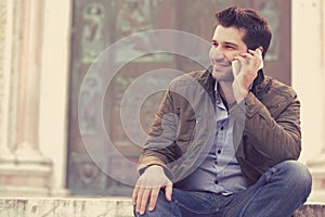 Man talking on a phone. Casual professional using smartphone smiling outside old building.