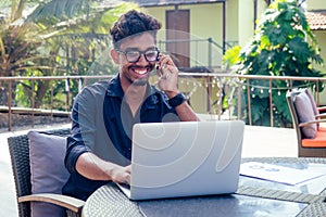 Man talking on the phone india summer holidays.stylish young indian male freelancer working with laptop freelance