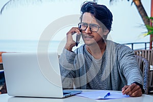 Man talking on the phone india summer holidays.stylish young indian male freelancer working with laptop freelance