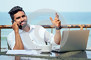 Man talking on the phone india summer holidays.stylish young indian male freelancer working with laptop freelance