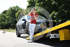 Man talking on phone near broken car and tow truck