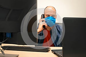 The man is talking on the phone in the office during quarantine. Virus protection at work. A specialist in a medical mask and a