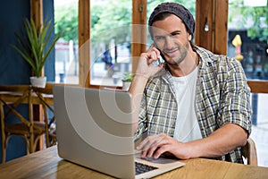 Man talking on phone while using laptop in coffee shop