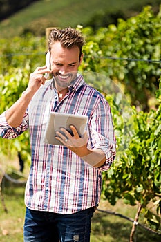 Man talking on phone while using tablet at vineyard
