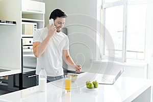 Man talking on smartphone near laptop and breakfast on kitchen table