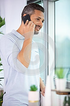 man talking on smartphone stood by window