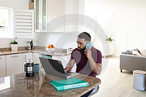 Man talking on smartphone while using laptop at home