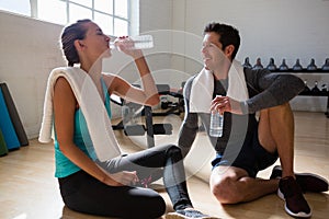 Man talking to female athlete drinking water while sitting in gym