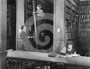 Man talking to a woman standing on a ladder in a library