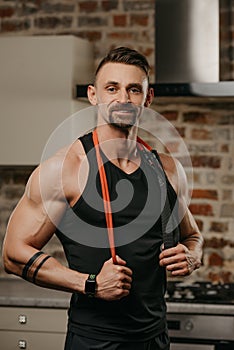 A man in a tank top with a pull elastic rope on the shoulders in his apartment