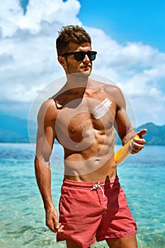 Man Tanning Using Sunscreen Cream On Body Skin. Summer