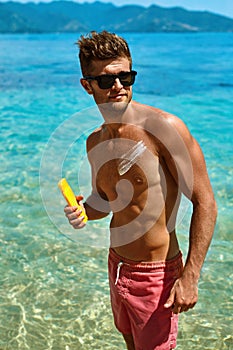 Man Tanning Using Sunscreen Cream On Body Skin. Summer