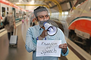 Man with taped mouth holding megaphone. Blurred metro subway station background.