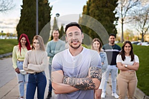 Man with tattooed arms smiling looking at the camera while standing in front of a group of people .