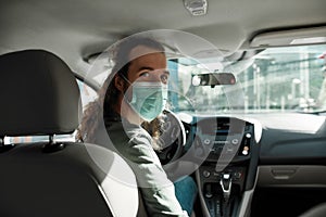 Man taxi driver talking to a passenger while steering the car during coronavirus pandemic wearing sterile medical mask