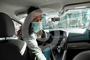 Man taxi driver talking to a passenger while steering the car during coronavirus pandemic wearing sterile medical mask