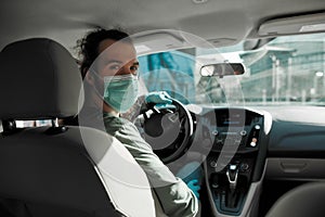 Man taxi driver talking to a passenger while steering the car during coronavirus pandemic wearing sterile medical mask