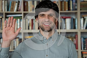 Man teacher in library looks camera communicates talk student on video call chat conference