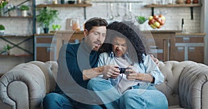 A man teaches his girlfriend to play a video game while sitting on the couch at home. The couple quarrels and shares the