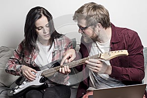 Man teaches a woman to play a six-string electric guitar.