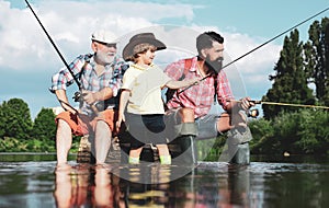 Man teaching kids how to fish in river. Grandfather, father and boy fishing together. Dad and son fishing at lake