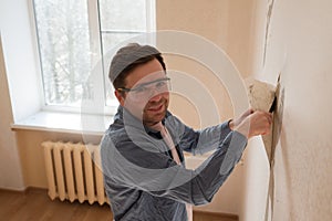 Man tearing off old wallpaper from wall preparing for home redecoration