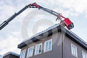 Man in the telescopic aerial platform cleaning snow and ice from roof top, gutter of the buliding to avoid the danger