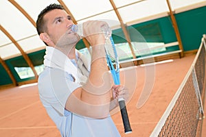 Man on tennis court drinking water