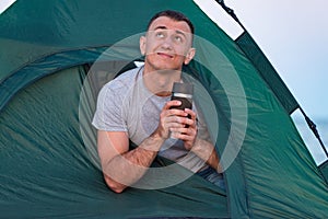 Man in tent drinks from tourist mug. Morning hike. Camping