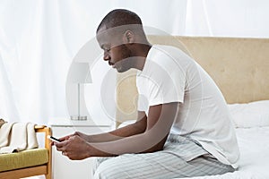 Man text messaging on mobile phone in bedroom