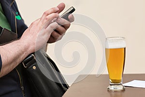 Man texting on his cell phone with a full glass of beer on the t