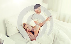 Man texting message while woman is sleeping in bed