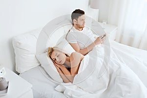 Man texting message while woman is sleeping in bed