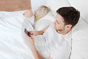 Man texting message while woman is sleeping in bed