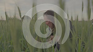 A man thanks God before eating, sitting in tall grass on a green wheat field.