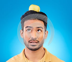 Man, thinking or balance apple on head in studio isolated on a blue background. Confused, fruit or Asian person with