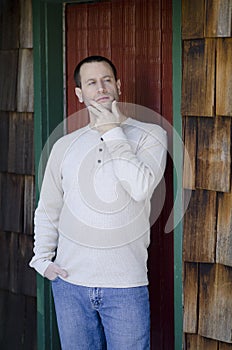 Man thinking by a cozy cabin door.