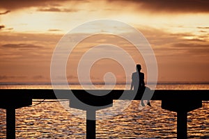 Man thinking on edge of pier at sunset