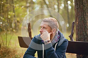 Man thinking moody portrait, sitting at autumn park