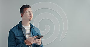 Man, thinking or typing on cellphone in studio, or notification on mobile app by gray background. Designer, planning and