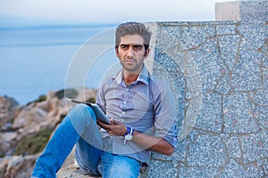 Man thinking using pad sitting on a concrete bridge above the sea