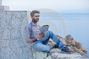 Man thinking using pad sitting on a concrete bridge above the sea