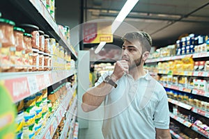 A man thinks what kind of product in a supermarket to choose. The buyer selects canned food at the store.