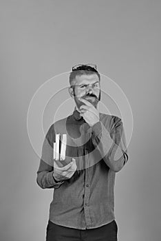 Man with thoughtful face and beard holds pile of books on blue background.