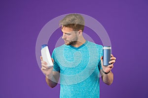 Man on thoughtful face chooses shampoo, violet background. Guy with bristle holds two bottles with shampoo, copy space