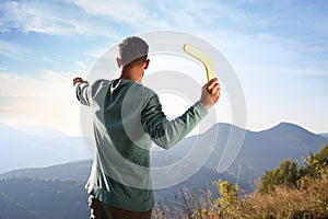 Man throwing boomerang in mountains on sunny day, back view photo