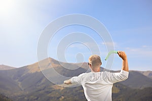 Man throwing boomerang in mountains on sunny day, back view. Space for text